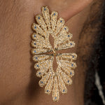 A woman wearing a pair of Cremilde Bispo Jewellery Guipure Topaz GP earrings with blue topaz gemstones.