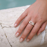 A woman's hand adorned with a Cremilde Bispo Jewellery Glade ring, nestled amidst a glade of floral foliage.