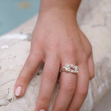 A woman's hand holding the Cremilde Bispo Jewellery Glade ring next to a pool surrounded by floral foliage.