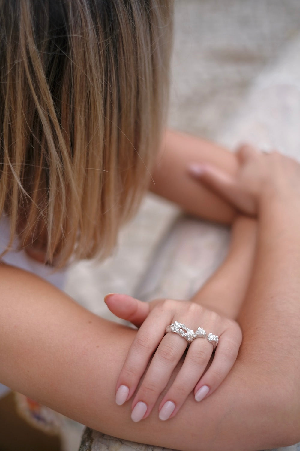 A woman wearing the Cremilde Bispo Jewellery's Glade ring adorned with floral foliage on her arm, standing in a glade.