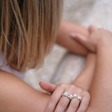 A woman wearing the Cremilde Bispo Jewellery's Glade ring adorned with floral foliage on her arm, standing in a glade.