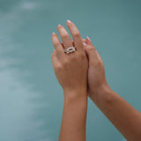 A handcrafted Glade ring adorned with floral foliage delicately held by a woman's hand near a serene pool in the glade, by Cremilde Bispo Jewellery.