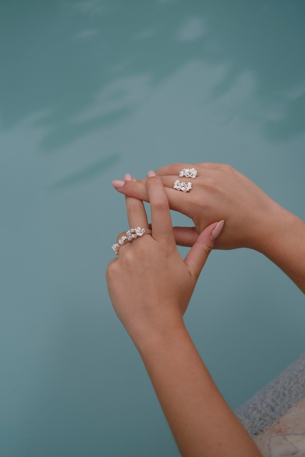 A woman's handcrafted hands adorned with a Cremilde Bispo Jewellery floral foliage jewelry collection, gently cradling The Glade ring by a pool.