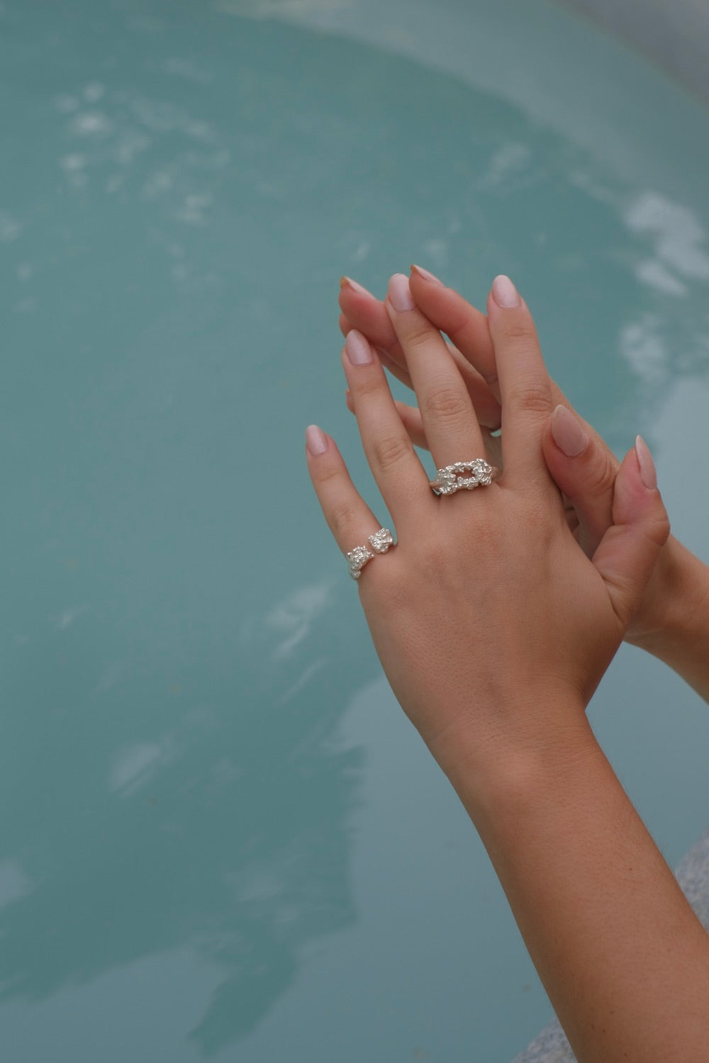 A woman's hand holding The Glade ring from her Cremilde Bispo Jewellery collection next to a pool.