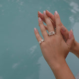 A woman's hand holding The Glade ring from her Cremilde Bispo Jewellery collection next to a pool.