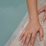 A woman's hand adorned with a handcrafted gold Glade ring from the Cremilde Bispo Jewellery collection, showcased elegantly next to a pool.