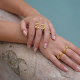 A woman's hand adorned with two gold rings from the Cremilde Bispo Jewellery Glade ring GP collection, glistening under the sunlight next to a pool.