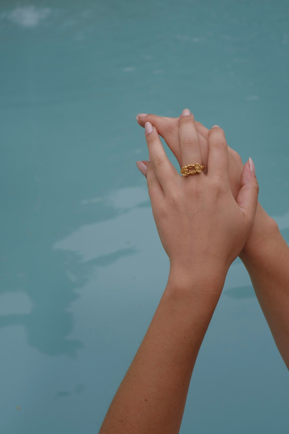 A woman's hand holding a gold ring from the Cremilde Bispo Jewellery Glade ring GP collection in the water.