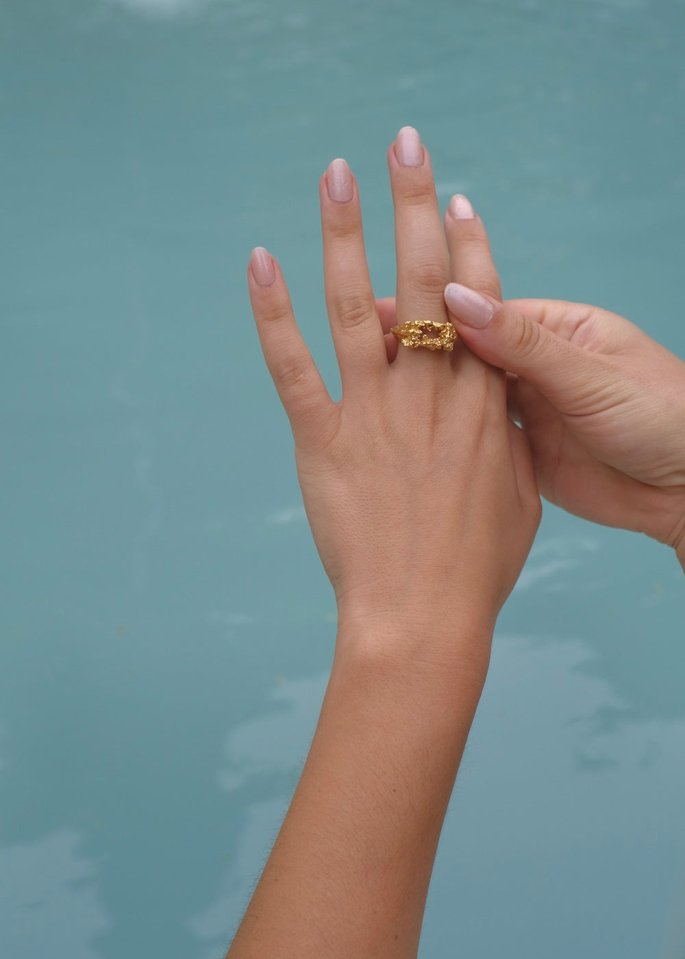 A handcrafted woman's hand holding the Glade ring GP by Cremilde Bispo Jewellery next to a pool.