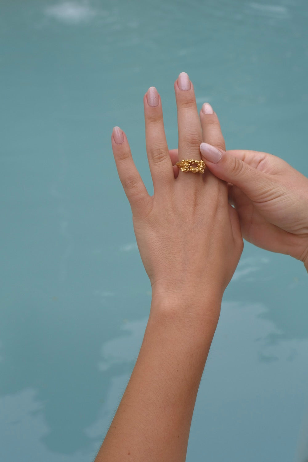 A handcrafted woman's hand holding the Glade ring GP by Cremilde Bispo Jewellery next to a pool.