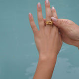 A handcrafted woman's hand holding the Glade ring GP by Cremilde Bispo Jewellery next to a pool.