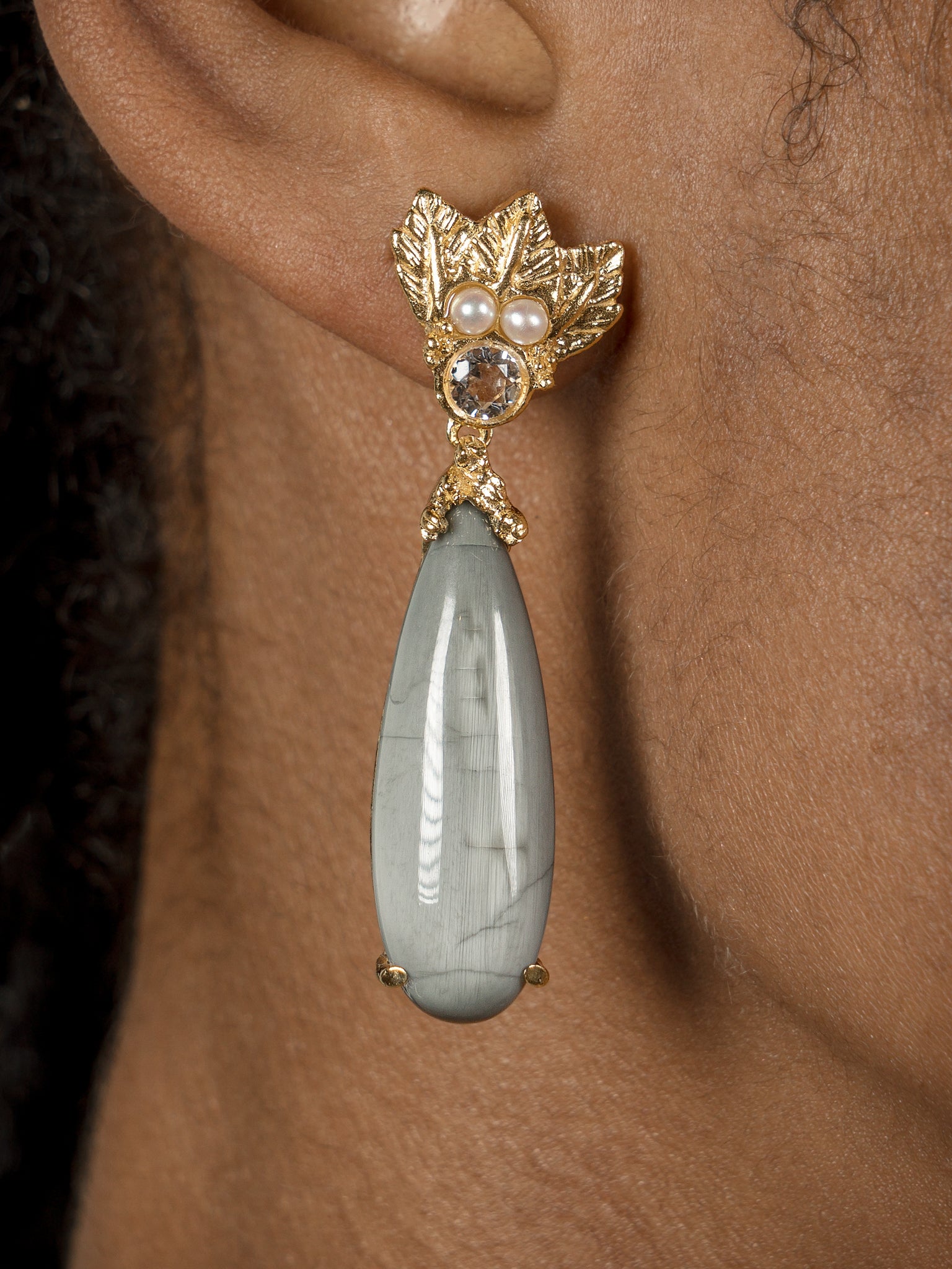 A woman wearing a pair of Cremilde Bispo Jewellery Muse III Toed eye earrings with a green stone.