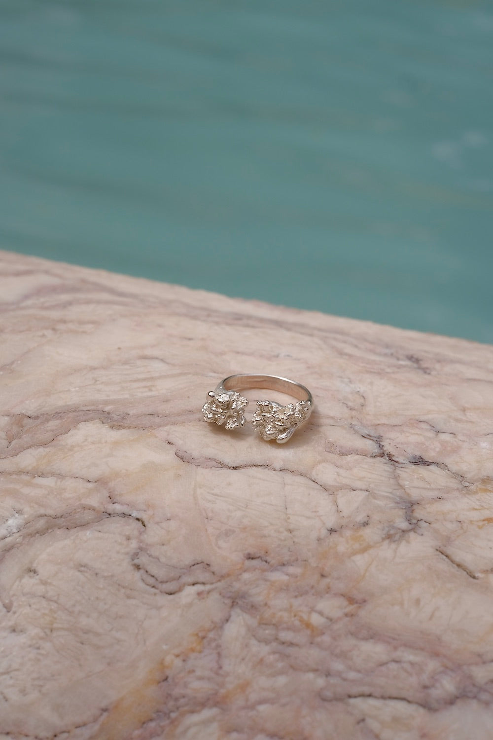 A handcrafted gold ring from Lisbon Atelier elegantly adorns the surface of a marble pool, exuding the splendor of the Cremilde Bispo Jewellery Valley ring.