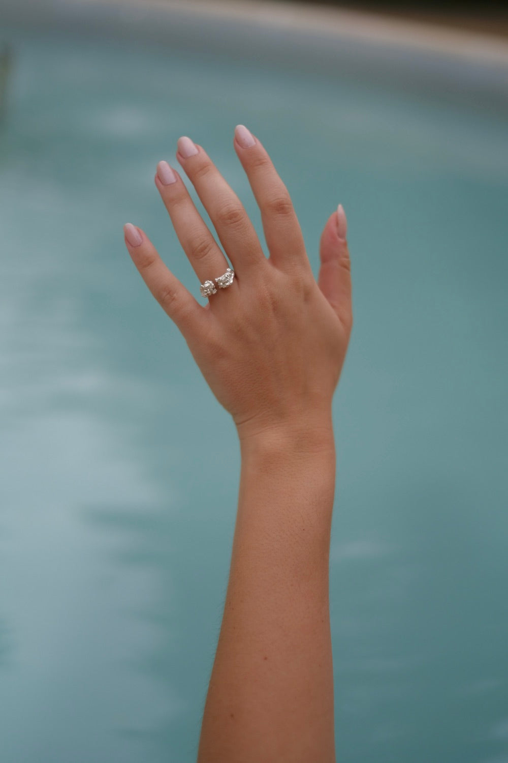 A woman's hand in Lisbon Atelier pool with a Cremilde Bispo Jewellery Valley ring on it.