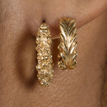 A close up of a woman's ear adorned with Cremilde Bispo Jewellery's Essential Leaf Hoops GP gold hoop earrings.