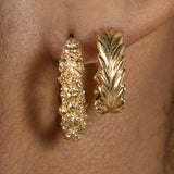 A close up of a woman's ear adorned with Cremilde Bispo Jewellery's Essential Leaf Hoops GP gold hoop earrings.