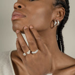 A black woman exuding maximum style while wearing Cremilde Bispo Jewellery's Essential Leaf Hoops and a set of silver rings.