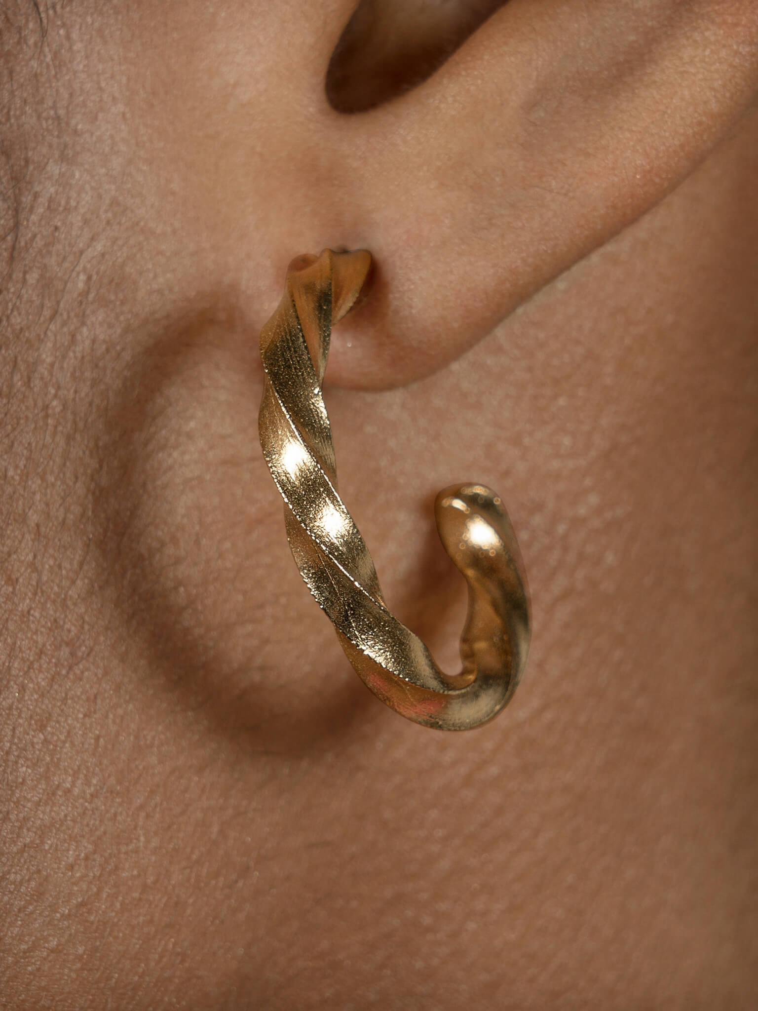 A close-up photo of a woman's hear featuring the Essential Twisted Hoops by Cremilde Bispo Jewellery in Gold Plated Silver.