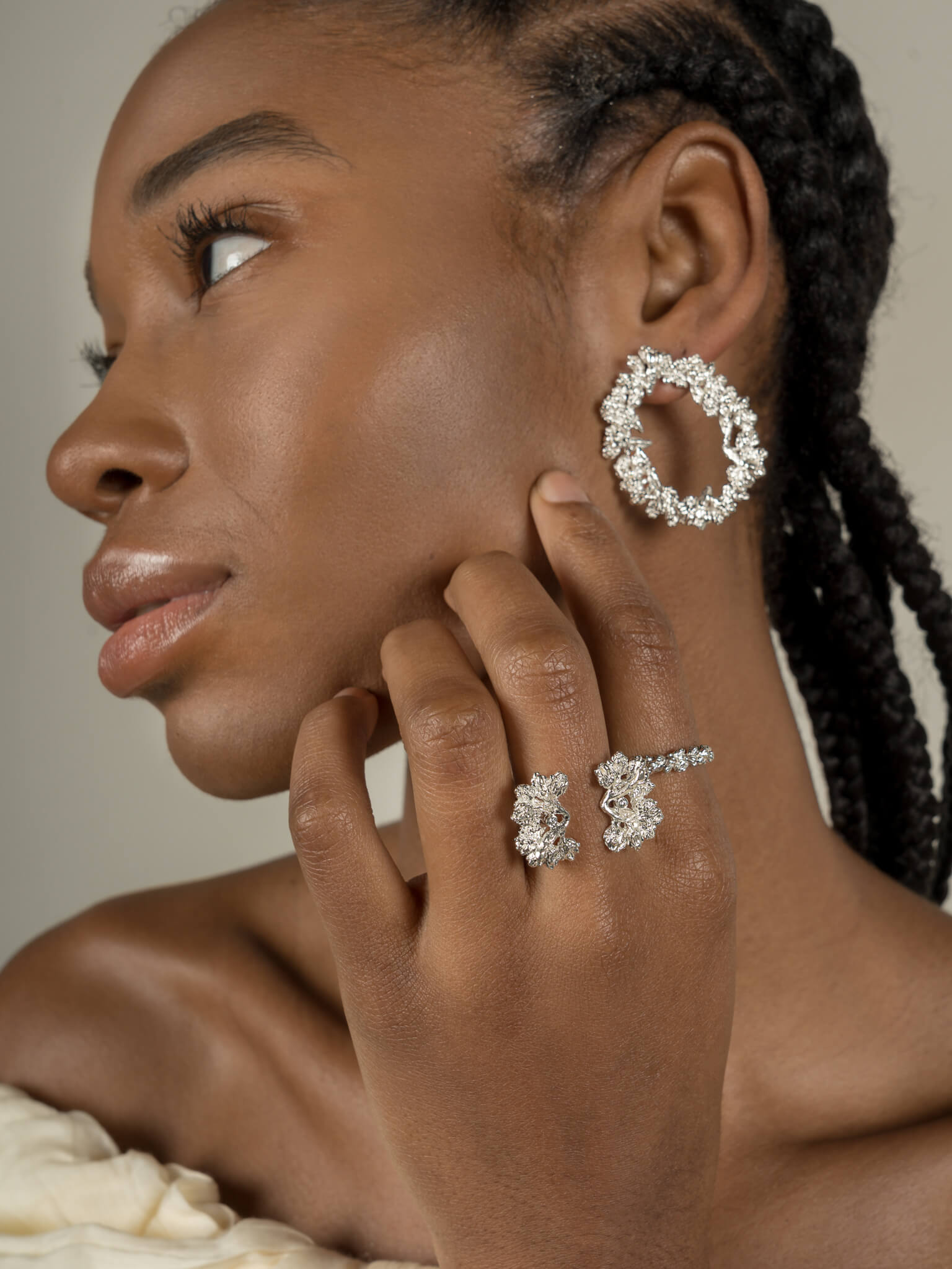 A black woman wearing a pair of handcrafted earrings adorned with floral foliage and The Garden Ring in sterling silver, embedded with Quartz, from Cremilde Bispo Jewellery.