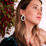 A refined woman is posing in front of a Christmas tree, showcasing the Cremilde Bispo Jewellery's Garden's Delight earrings, in sterling silver, which perfectly complement nature's beauty.