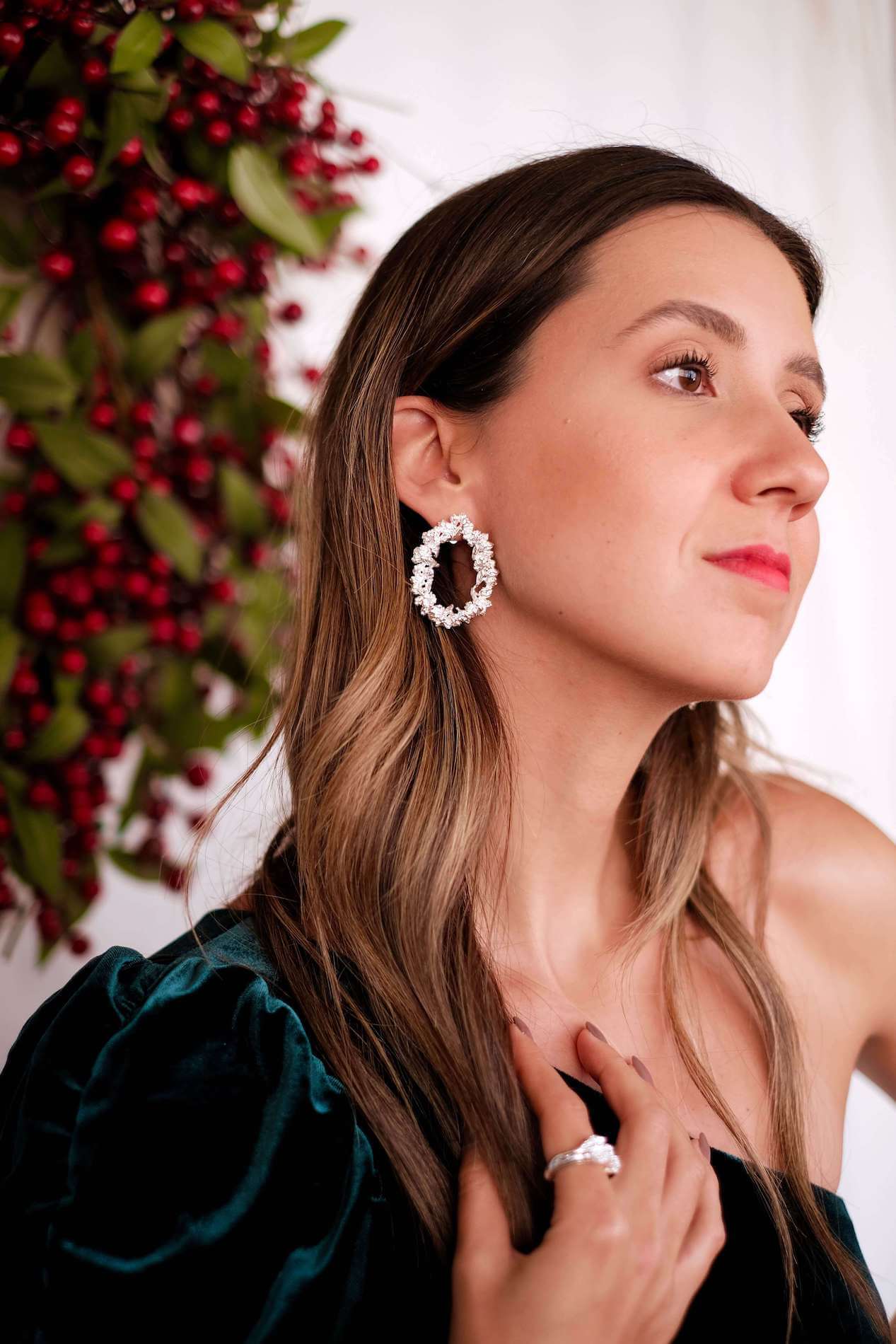 A refined woman is posing in front of a Christmas tree, showcasing the Cremilde Bispo Jewellery's Garden's Delight earrings, in sterling silver, which perfectly complement nature's beauty.