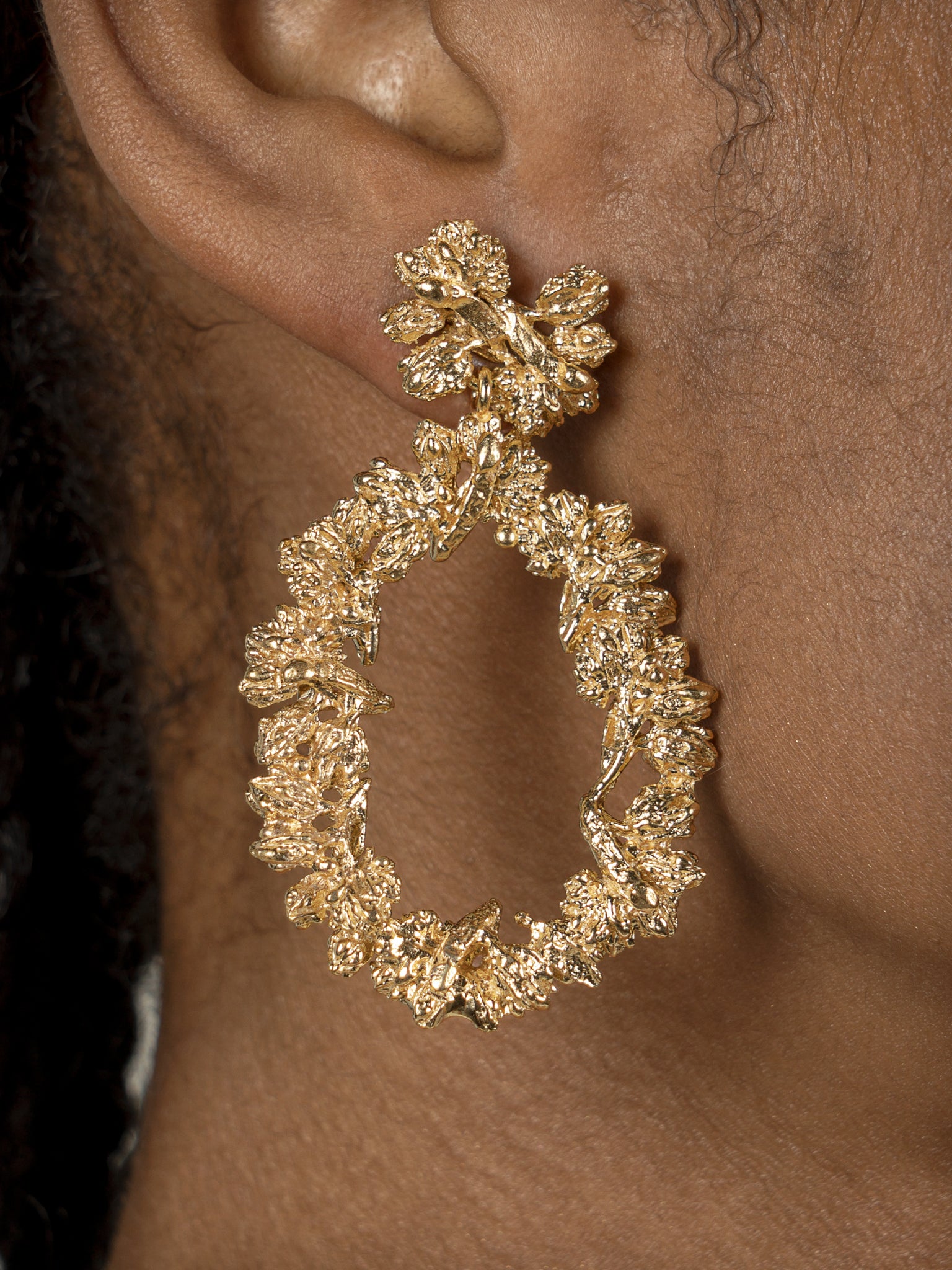 A woman showcasing opulence with a Cremilde Bispo Jewellery gold hoop earring, The Garden's Delight II GP.