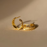 Cremilde Bispo Jewellery's Essential Leaf Hoops GP, resting on a beige surface, exude timeless elegance and an exclusive touch.