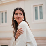 A woman wearing a white sweater and Cremilde Bispo Jewellery's Pearly Forest Earrings, standing on a balcony.