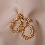 A pair of The Garden's Delight II GP hoop earrings by Cremilde Bispo Jewellery on a beige fabric.