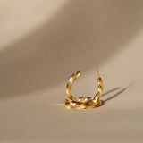 A fashionable woman's Essential Twisted Hoops GP earring by Cremilde Bispo Jewellery on a beige surface.