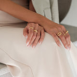 A woman, adorned with Cremilde Bispo Jewellery's hand-carved floral foliage gold rings, elegantly displays the timeless beauty of Ancient Rome's grandeur in her white dress. The Laurel Ring GP.