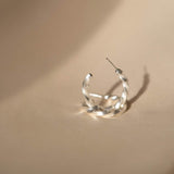 A fashionable woman's Cremilde Bispo Jewellery Essential Twisted Hoops earring, made of sterling silver, sitting on top of a table.