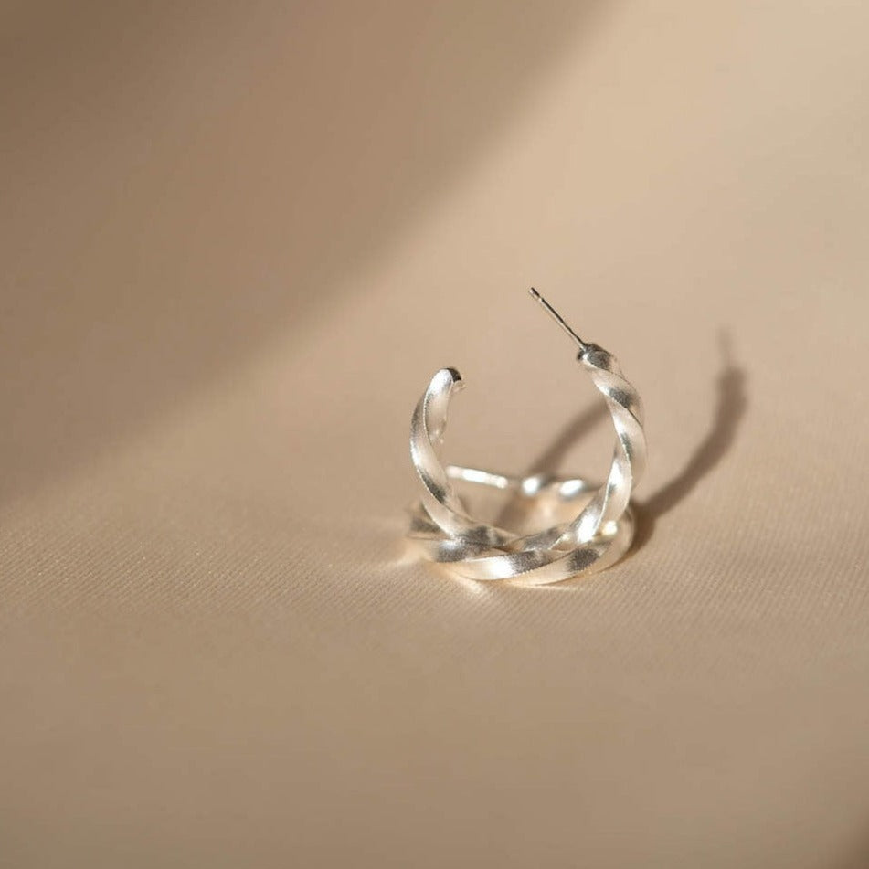 A fashionable woman's Cremilde Bispo Jewellery Essential Twisted Hoops earring, made of sterling silver, sitting on top of a table.