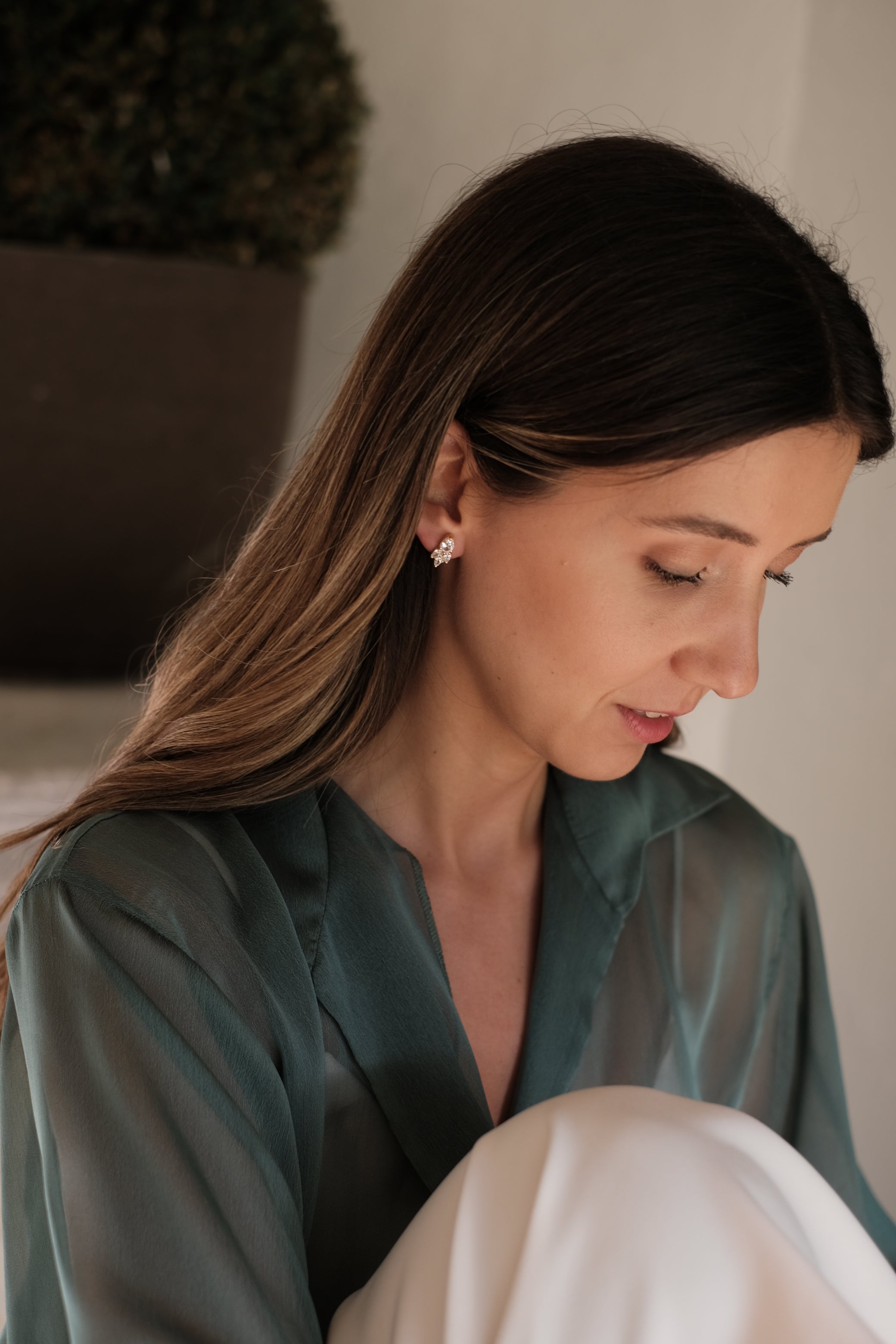 A woman in Lisbon is sitting on a bed, engrossed in her phone while wearing the stunning Cremilde Bispo Jewellery Essential Drops earrings from her jewelry collection.