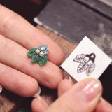 A person is holding The Muse I, a handcrafted jewelry piece by Cremilde Bispo Jewellery, with a leaf on it.