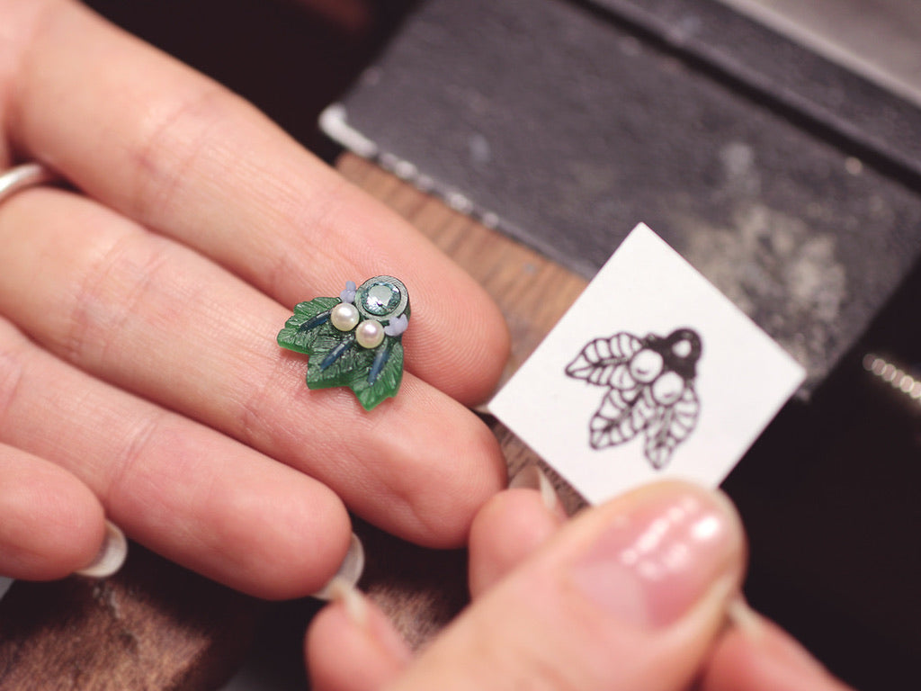 A person is holding The Muse I, a handcrafted jewelry piece by Cremilde Bispo Jewellery, with a leaf on it.