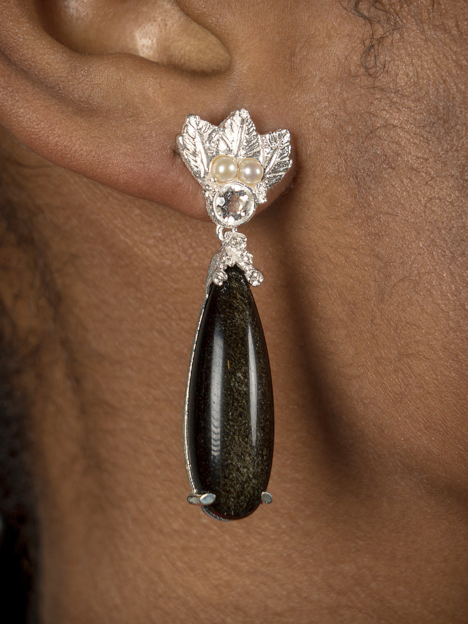 An elegant woman wearing a pair of The Muse III Obsidian earrings by Cremilde Bispo Jewellery, showcasing exquisite jewelry.