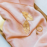 A vintage-inspired Guipure GP gold leaf ring and a pink silk scarf, delicately arranged on a tray by Cremilde Bispo Jewellery.