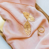 A vintage-inspired Guipure GP gold leaf ring and a pink silk scarf, delicately arranged on a tray by Cremilde Bispo Jewellery.