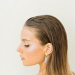 A woman in a white dress is wearing a pair of earrings adorned with The Muse III Chalcedony from Cremilde Bispo Jewellery.