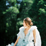 A vintage-inspired bride in a blue tulle dress sitting on a railing, adorned with elegant Cremilde Bispo Jewellery's Guipure GP lace artistry.