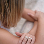 A woman wearing the Cremilde Bispo Jewellery's Glade ring adorned with floral foliage on her arm, standing in a glade.
