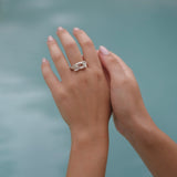 A woman's hand holding a Cremilde Bispo Jewellery Glade ring in front of a pool with glade floral foliage.
