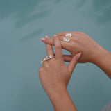 A woman's handcrafted hands adorned with a Cremilde Bispo Jewellery floral foliage jewelry collection, gently cradling The Glade ring by a pool.