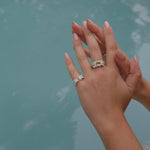 A woman's hand holding The Glade ring from her Cremilde Bispo Jewellery collection next to a pool.