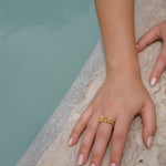 A woman's hand adorned with a handcrafted gold Glade ring from the Cremilde Bispo Jewellery collection, showcased elegantly next to a pool.