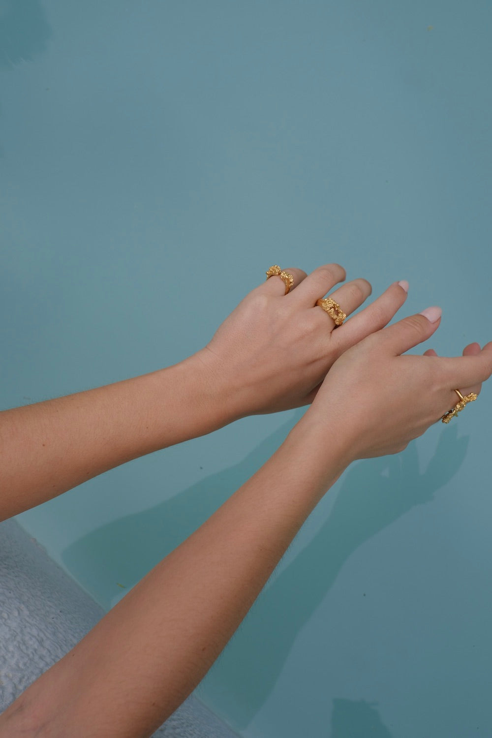 A woman's handcrafted hands in a pool with gold rings on them featuring the exquisite Glade ring GP from her dazzling Cremilde Bispo Jewellery collection.