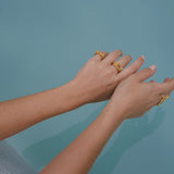 A woman's handcrafted hands in a pool with gold rings on them featuring the exquisite Glade ring GP from her dazzling Cremilde Bispo Jewellery collection.