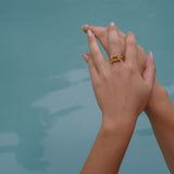 A woman's hand holding a gold ring from the Cremilde Bispo Jewellery Glade ring GP collection in the water.
