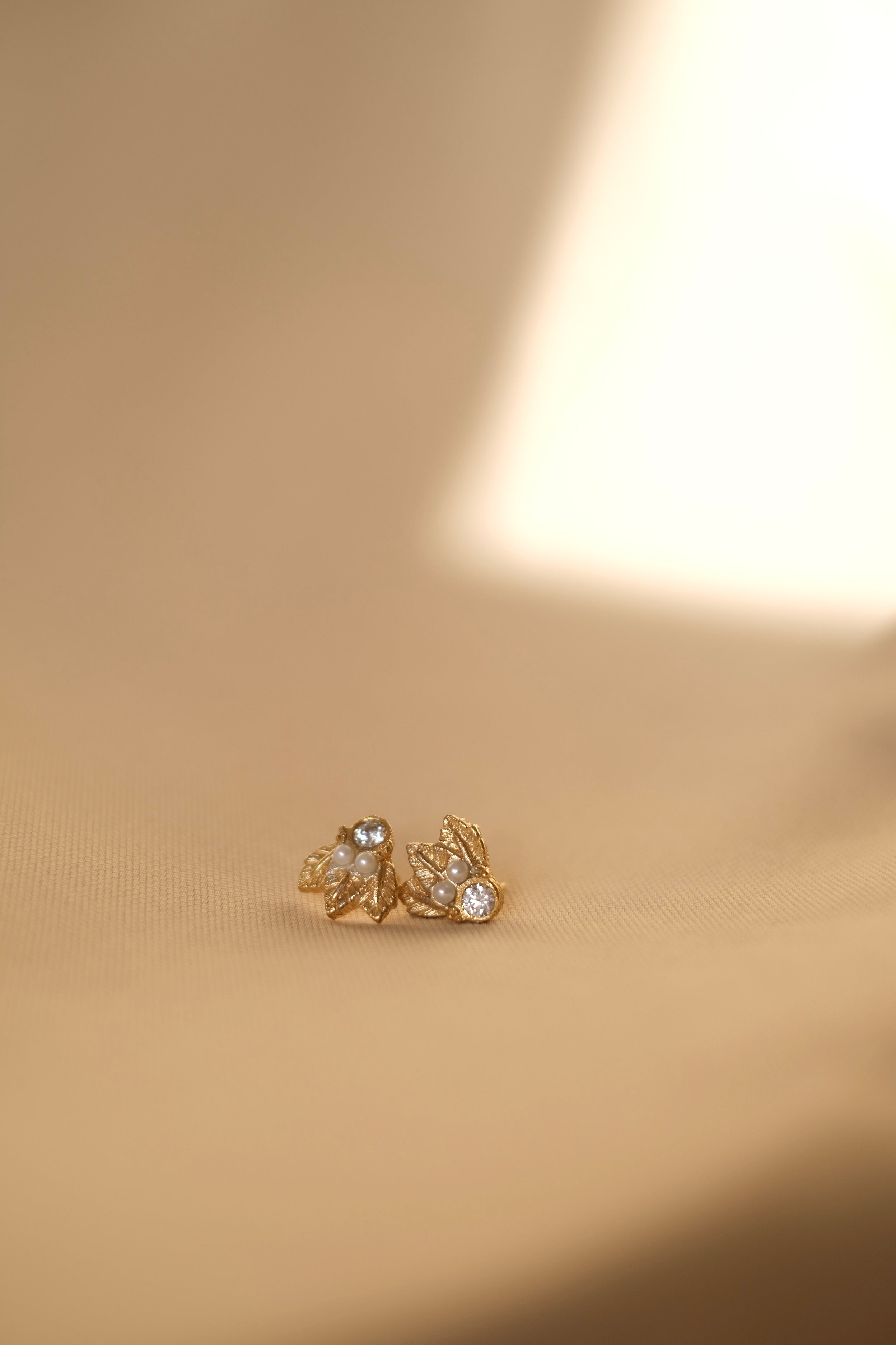 A pair of handcrafted The Muse I GP gold stud earrings on a beige background by Cremilde Bispo Jewellery.